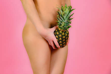 A young and sexy girl is holding a pineapple near the feet, on a pink background.の写真素材