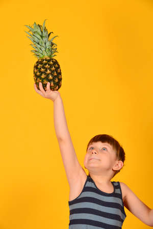 The boy is holding a pineapple above his head, on an outstretched hand on a yellow background.の写真素材