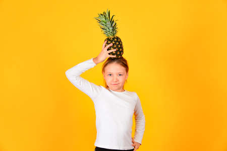 A girl in white is holding a pineapple on her head, on a yellow background.