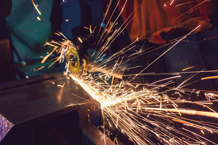 The worker cuts the workpiece with an electric grinder, many sparks fly sideways