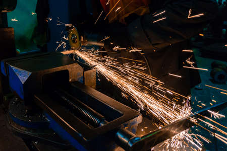 The worker cuts the workpiece with an electric grinder, many sparks fly sideways