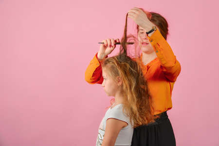 Young woman doing hairstyle girl, in the studio on a pink background.の写真素材