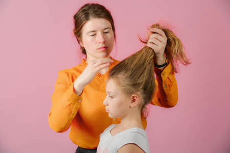 Young woman doing hairstyle girl, in the studio on a pink background.