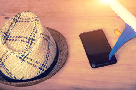 Straw hat, toy plane and smartphone lie on a wooden texture, concept of travel, vacation and summer...