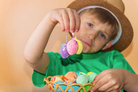 A boy in a straw hat holds painted Easter eggs in his hand.