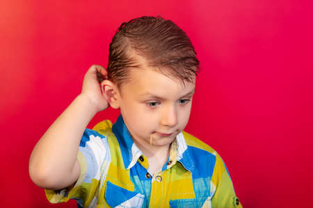 A boy in a colored shirt is scratching his head in suspense, on a red background.