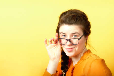 Girl holds glasses with hand on yellow background, concept of office employee about to leave