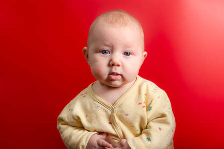 Portrait of a baby on a red background, newborn girl close-up in the studio.