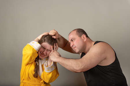 The husband beats his wife with a fist and tears her hair, a staged photo.