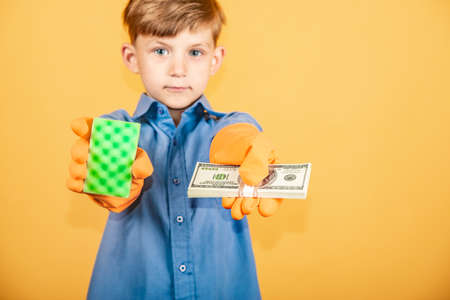 A handsome boy in a blue shirt and washing gloves holds a pack of dollars in one hand and a washing sponge in the other and offers the viewer a choice.の写真素材