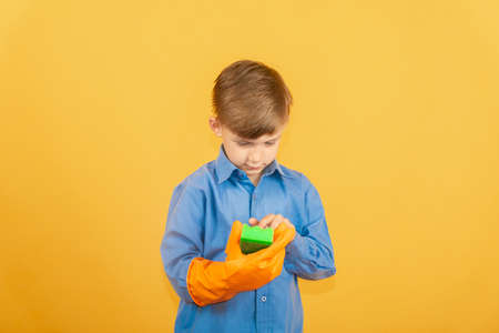 A boy in a blue shirt and orange gloves examines a green washing sponge.の写真素材