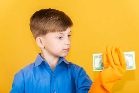 A handsome boy in washing gloves holds a wad of dollars in one hand and looks at it. The concept of money laundering and tax evasion.の写真素材