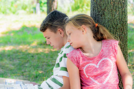 A boy and a girl are engaged in education, classmates together read from one textbook, the book lies on the grass.の写真素材