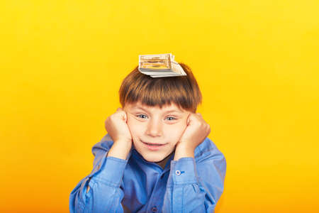 The boy holds money on his head, dollars lie on the childs head, but he doesnt know what to do with them.の写真素材