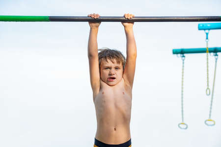 A little boy is hanging on the horizontal bar and can not do anything.の写真素材