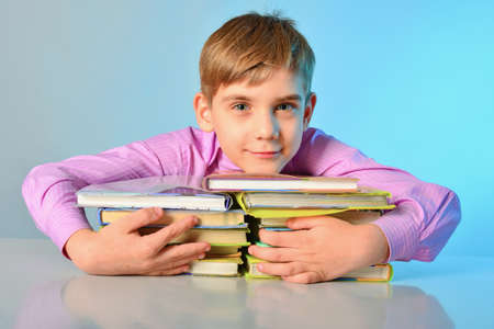 An inquisitive teenager hugs books while sitting at a desk.の写真素材