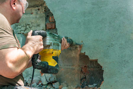 Dismantling walls and openings with an electric jackhammer. The worker in goggles performs repair work.の写真素材