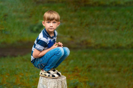 A boy in blue jeans squats in the park looking around.の写真素材
