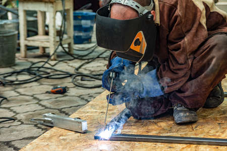 A welder at work assembles a metal structure from a shaped pipe.