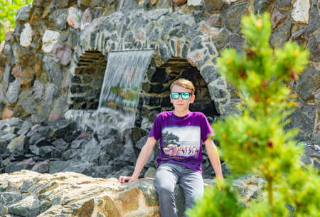 A child at the waterfall in the park, a boy in the reserve on the background of the flowing water in the park.の写真素材