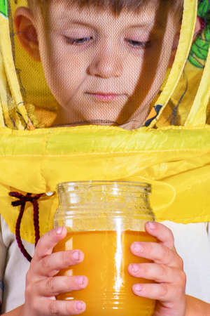 A boy in a protective yellow suit from bees holding a jar of honey in his hands. Isolated photo.の写真素材