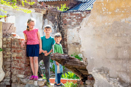 Poor orphans against the background of destroyed buildings, the concept of the life of street children. Staged photo.の写真素材