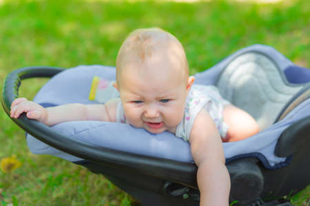 A child in a cradle in the park, a small child is trying to get out of the baby carriage.
