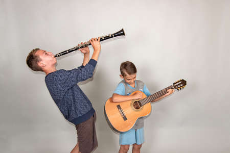 The boy plays the guitar and clarinet in different poses, posing in the studio.の写真素材