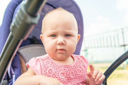 A child in a pushchair outside in the park, a little girl looks into the camera.の写真素材