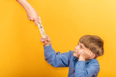 The boy in the blue shirt stretches out his hand and takes the dollars.