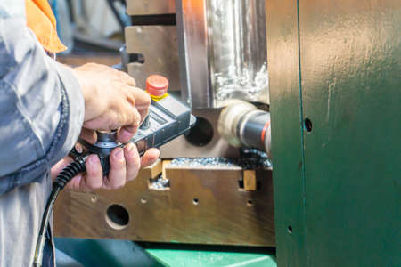 The worker controls the remote control on a cnc machine for milling and manufacturing the product.