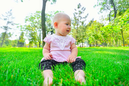 A joyful and happy little girl sits on the green grass and looks around.の写真素材