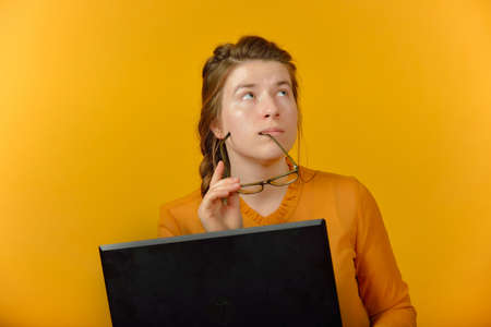girl in glasses and with a laptop on a yellow backgroundの写真素材