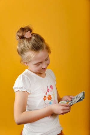 Little girl counts money in hands while thinking about shopping, on yellow background.の写真素材