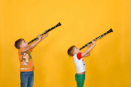 Two boys play the clarinet and hold it up, on a yellow background.の写真素材