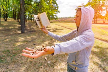 A man reads a book in the park, letters fly from above and fall on his hand, exhaustive knowledge in nature.の写真素材