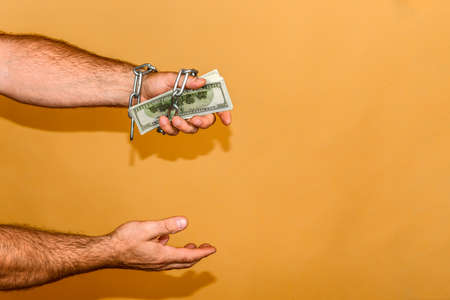 Man's hand is wrapped in a chain, holds dollars. The concept of monetary and financial dependence.の写真素材