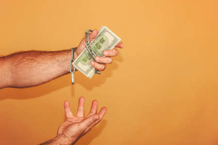 Man's hand is wrapped in a chain, holds dollars. The concept of monetary and financial dependence.