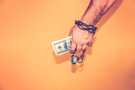 Man's hand is wrapped in a chain, holds dollars. The concept of monetary and financial dependence.の写真素材