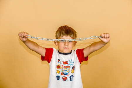 The boy holds a chain in his hands in front of his face.