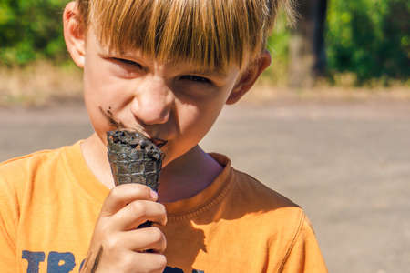 Black ice cream in the hands of a child, the boy eats black ice cream, dirty face and mouth.