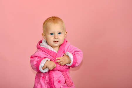 Little cute girl in a pink bathrobe on a pink background.の写真素材