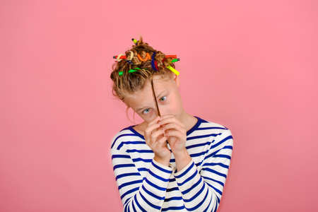 A girl with a funny hairstyle in a striped T-shirt touches her hair, is surprised and makes funny...