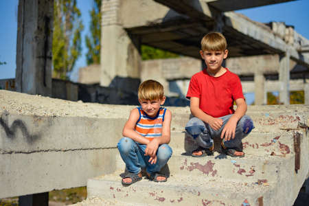 Two children are sitting on the steps of an abandoned building, a concept of the life of street children orphans.の写真素材