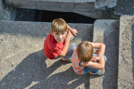 Two children are sitting on the steps of an abandoned building, a concept of the life of street children orphans.の写真素材