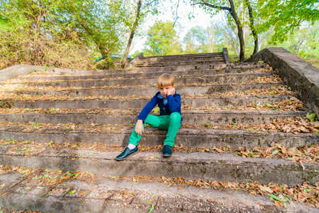 A boy sits on the old steps in the park, wide angle photo bottom view.
