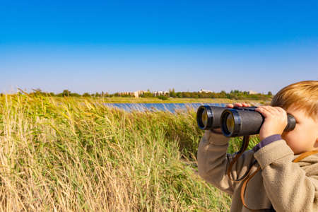 A boy with binoculars in the reeds is watching the wildlife.の写真素材