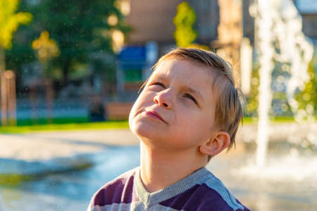Beautiful and cute boy smiles and poses on the background of the fountain