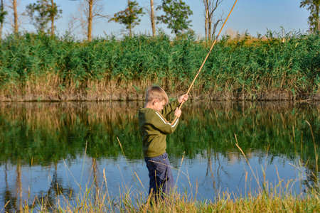 A boy holds a fishing rod over the water for fishing.の写真素材