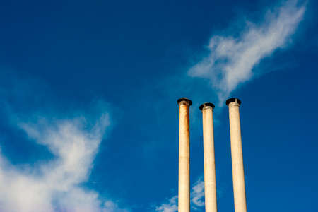 Three chimneys on a background of blue cloudy sky.